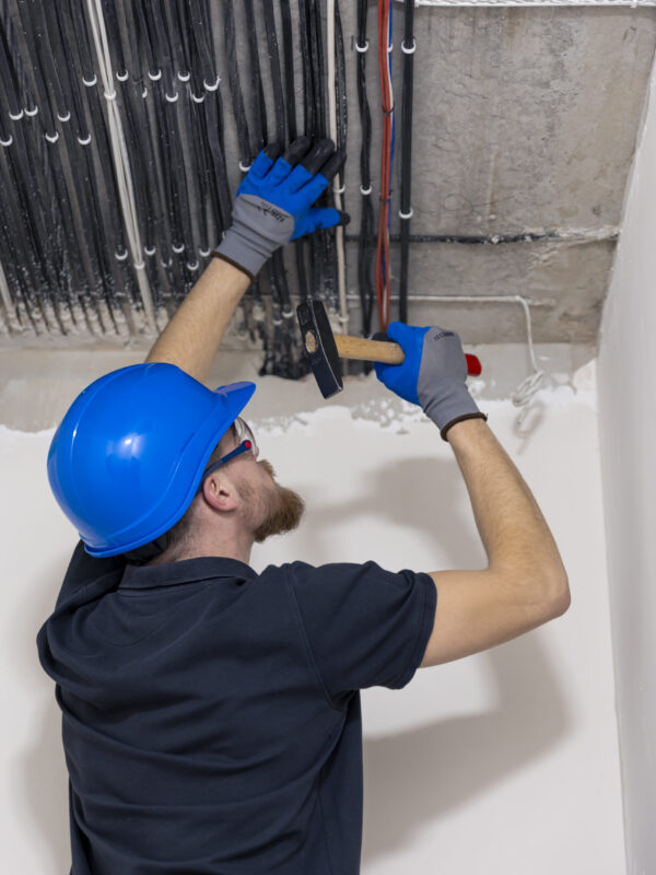 Electrician wearing a blue helmet, installing laying electrical cables on the ceiling inside the house under construction.